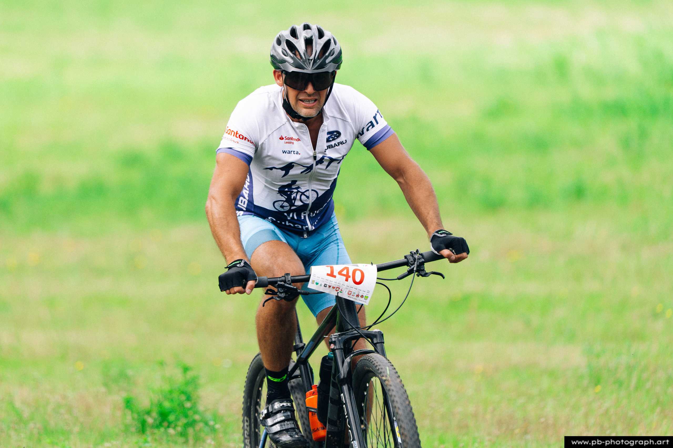 Zawodnik podczas wyścigu MTB w Szczecinie, na tle zielonej trawy, z numerem startowym na koszulce.