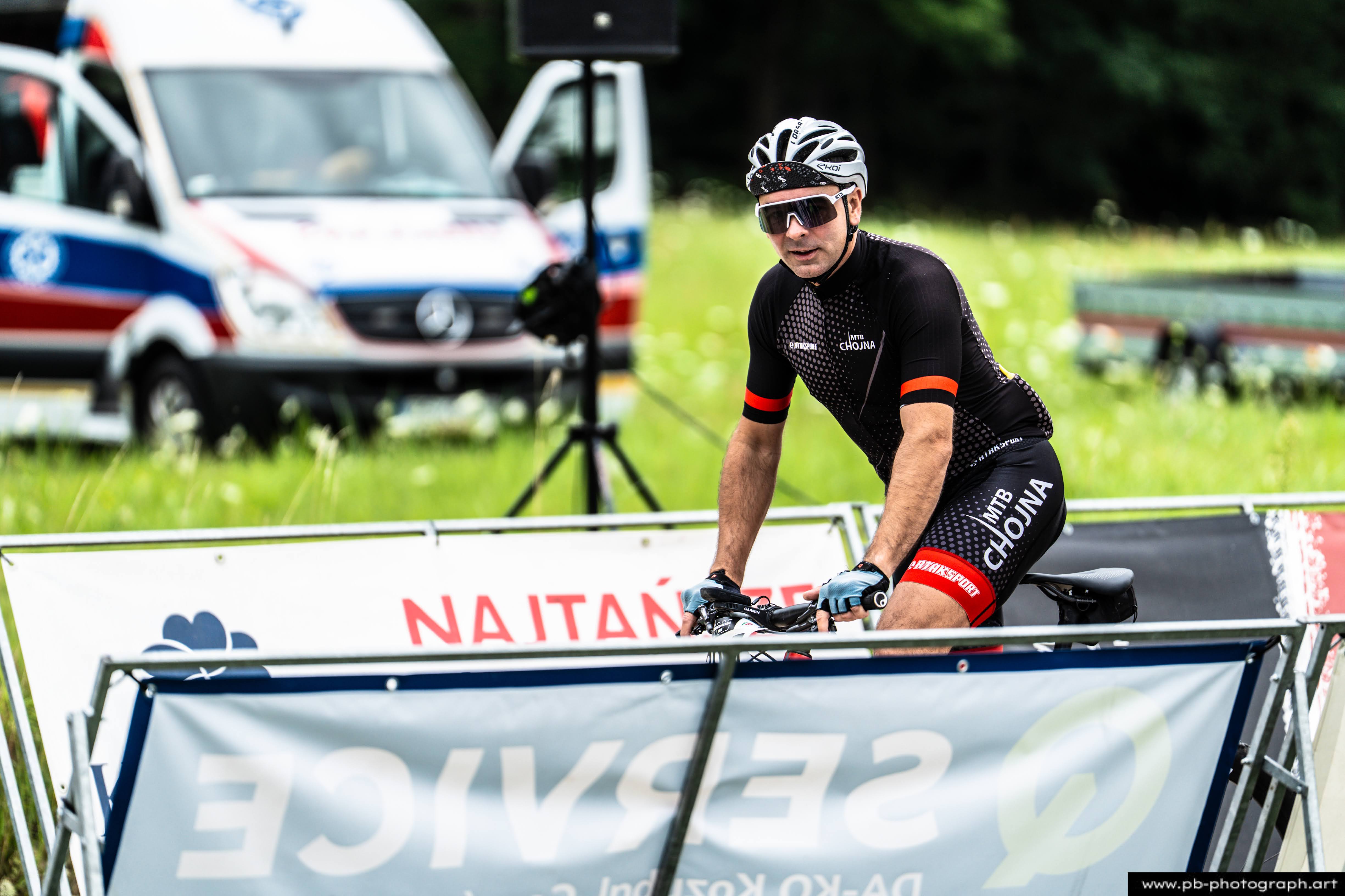 Zawodnik MTB na rowerze, przygotowujący się do startu w wyścigu w Szczecinie, z tłem strefy serwisowej.