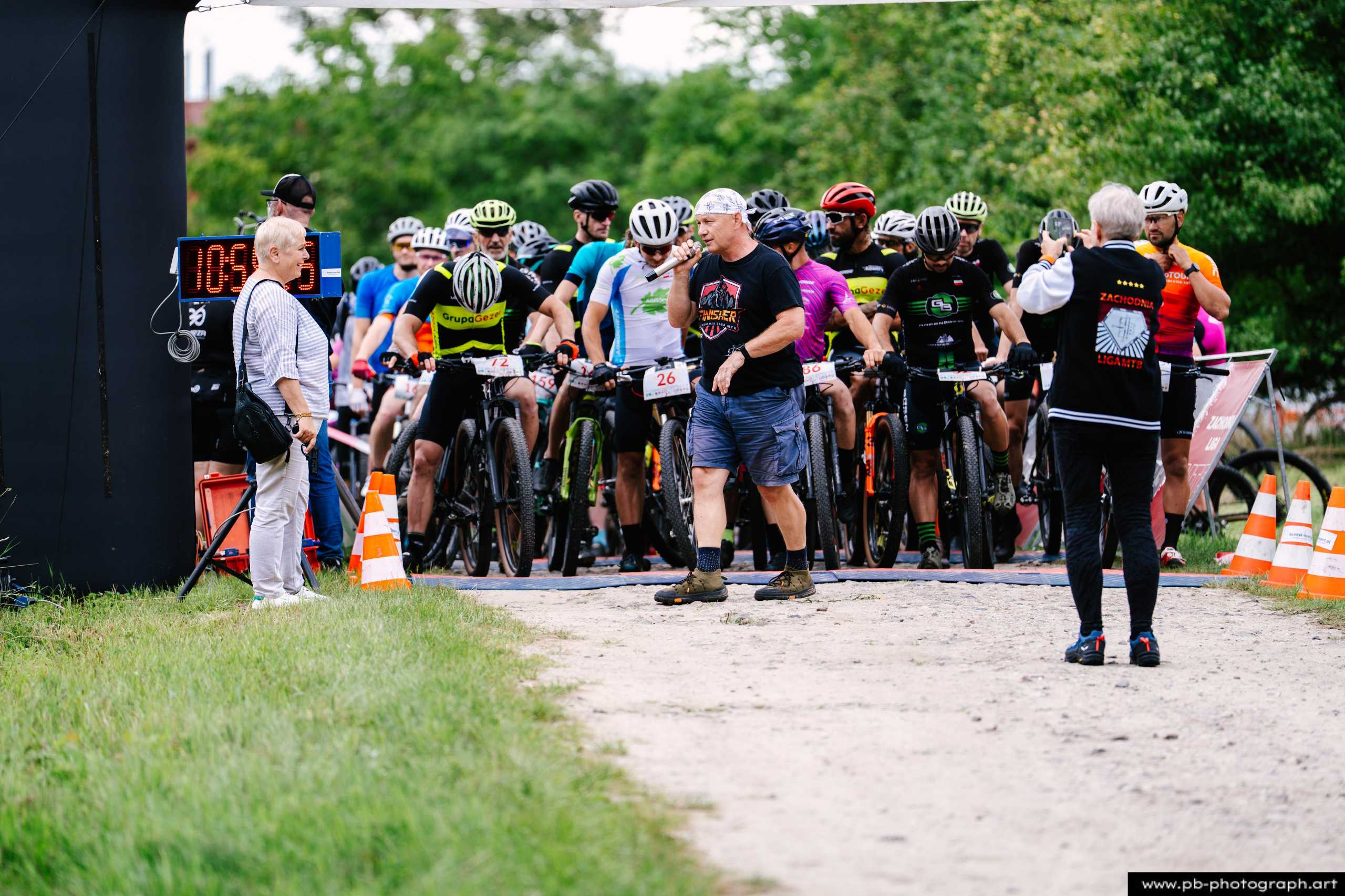 Zawodnicy przygotowujący się do startu wyścigu MTB na trasie w Szczecinie, z widocznym zegarem odliczającym czas.