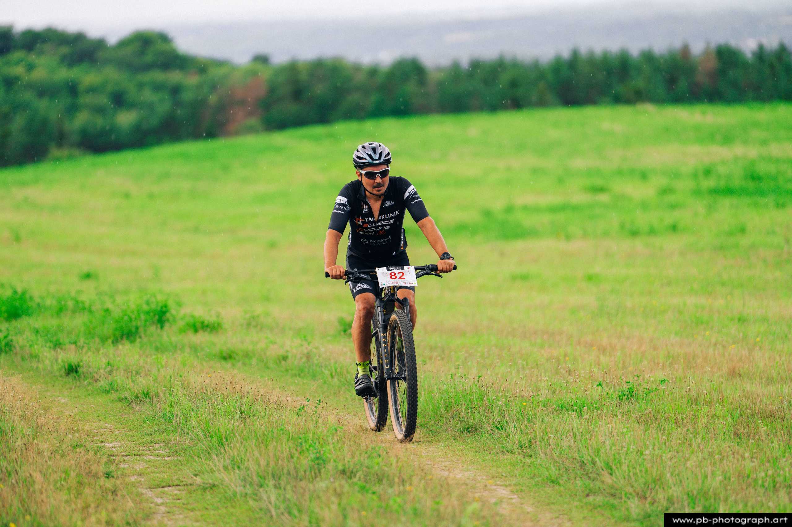 Zawodnik na rowerze górskim podczas wyścigu MTB w Szczecinie, na tle zielonego krajobrazu.