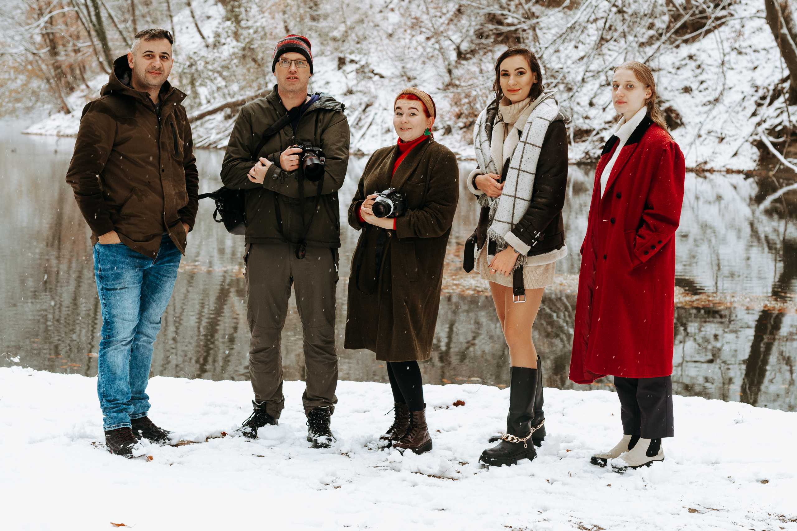 Grupa fotografów i modeli w zimowym plenerze w Szczecinie, otoczona śniegiem i drzewami przy wodzie.