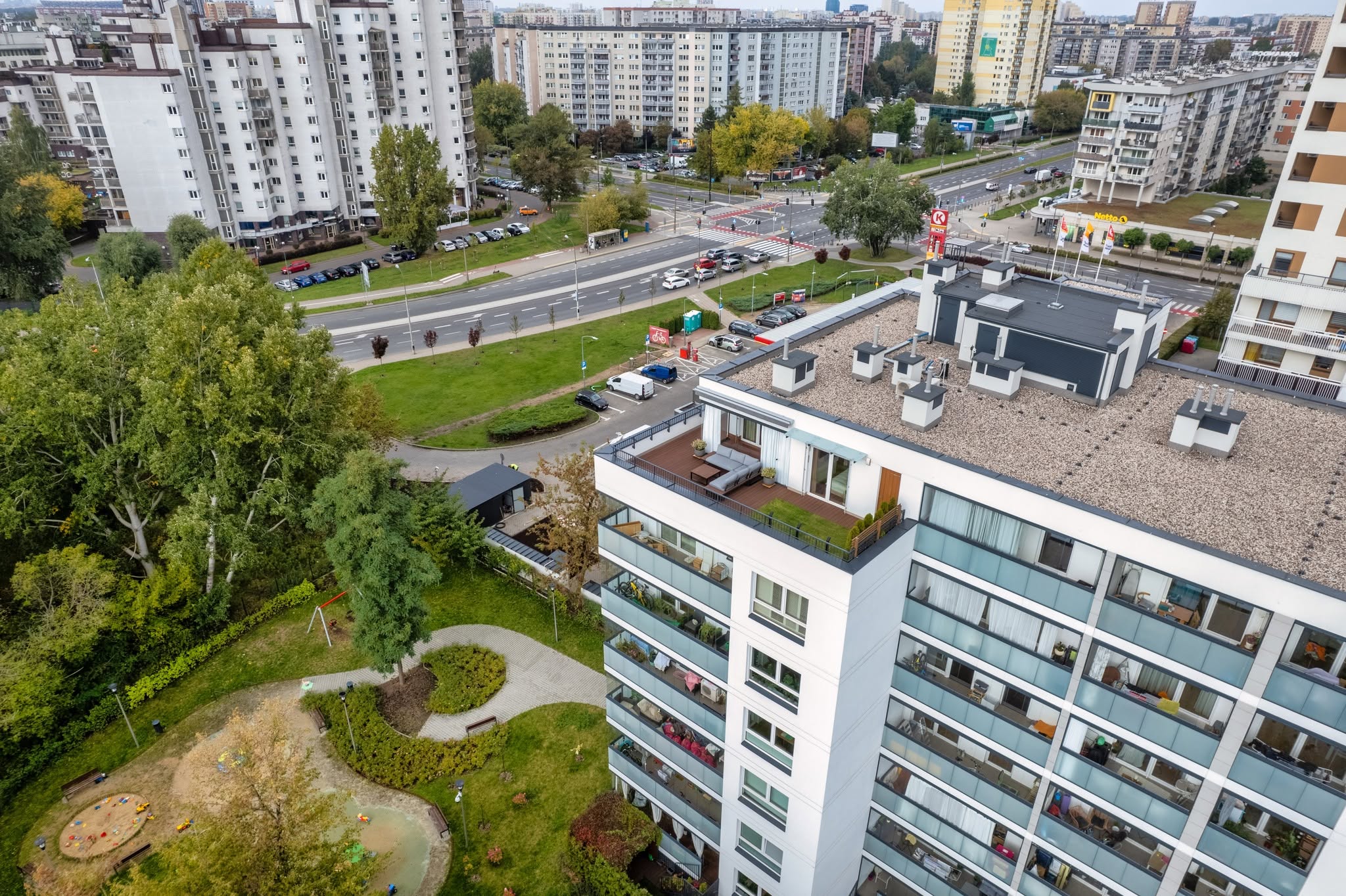 Widok na nowoczesny apartament z tarasem w Warszawie, otoczony zielenią i miejskim krajobrazem.
