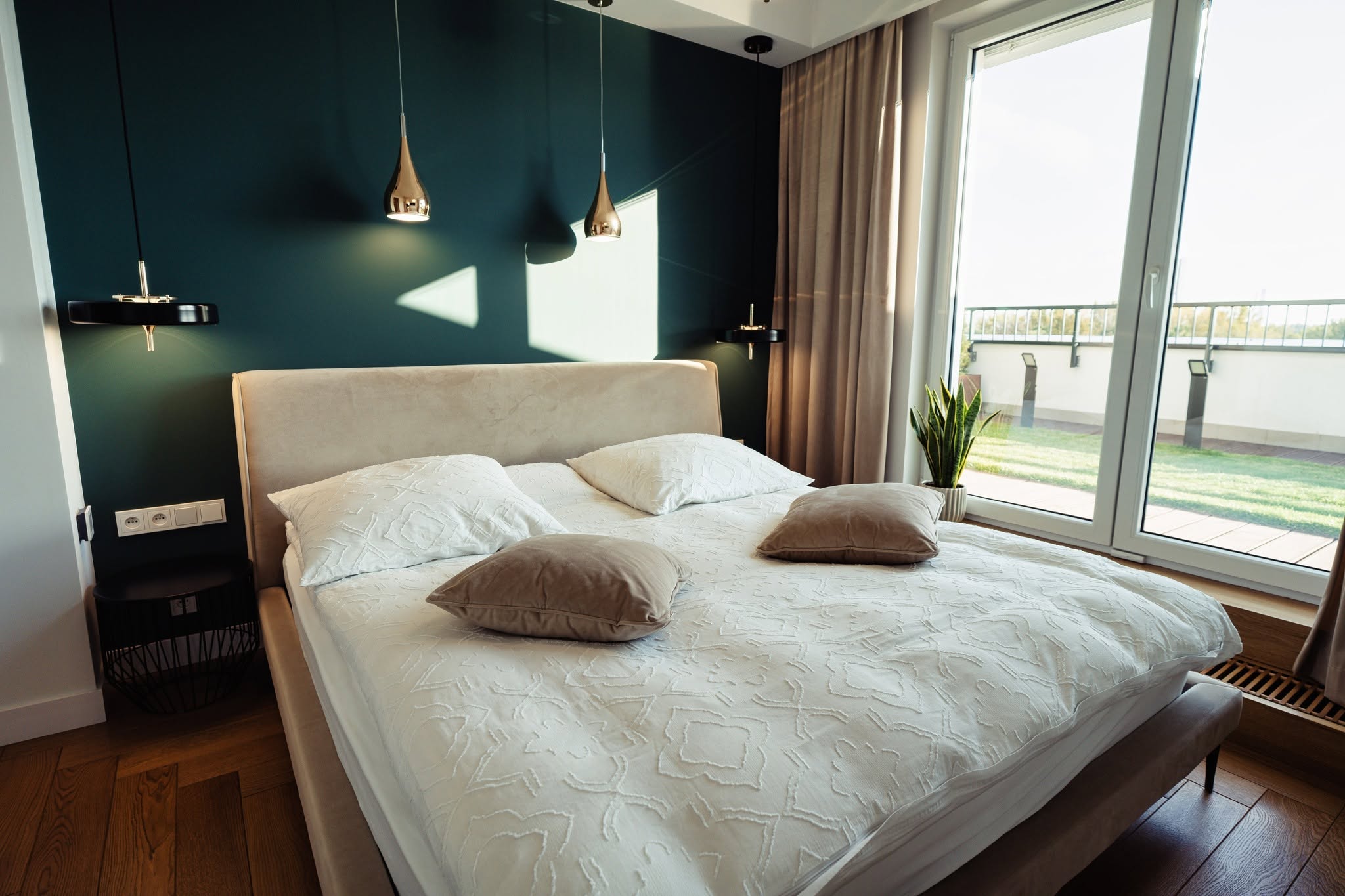 Elegancka sypialnia w apartamencie w Warszawie z podwójnym łóżkiem i dużymi oknami, wpuszczającymi naturalne światło.