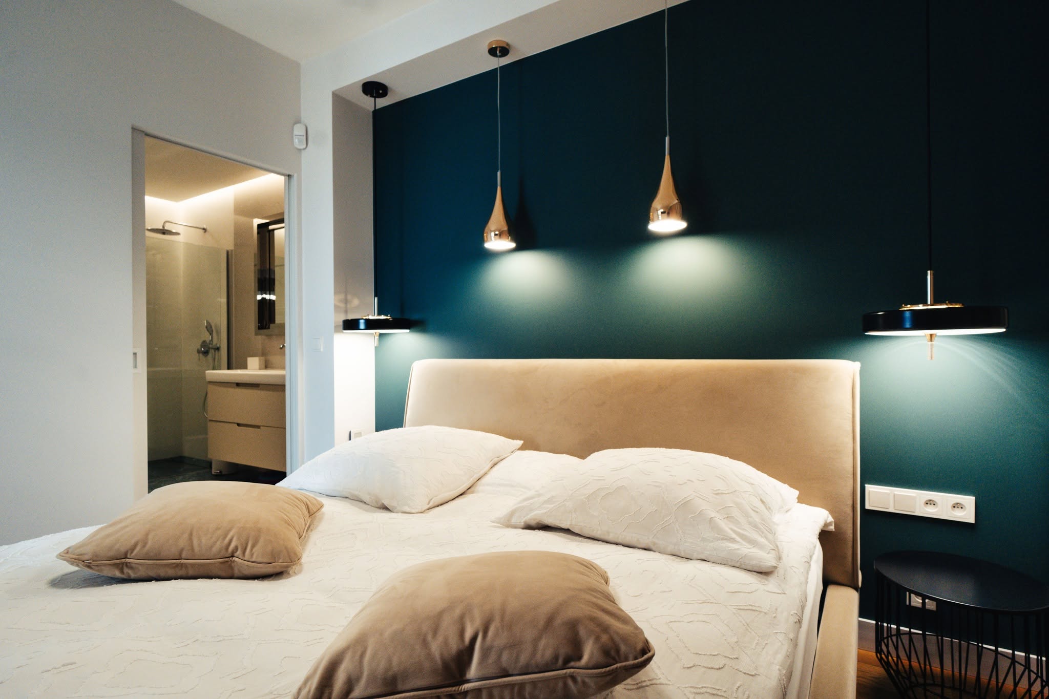Sypialnia w apartamencie z eleganckim łóżkiem i nowoczesnymi lampami na tle zielonej ściany.