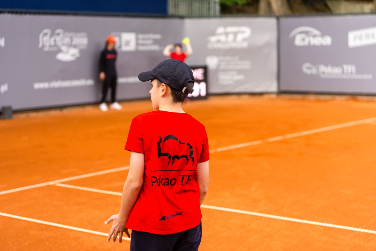 Chłopiec w czerwonej koszulce z logo na korcie tenisowym podczas turnieju Invest in Szczecin Open 2026.