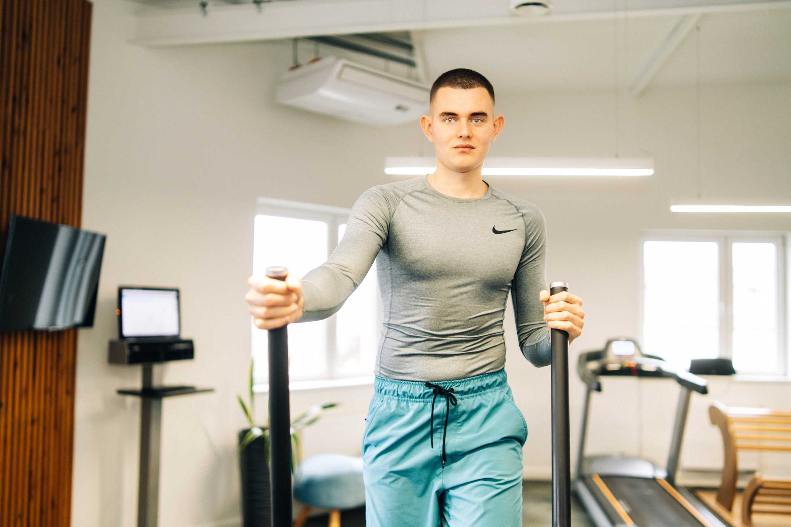 Trener w szarym stroju fitness, prowadzący ćwiczenia na sprzęcie w Klubie Fitnes 3L w Mierzynie, Szczecin.