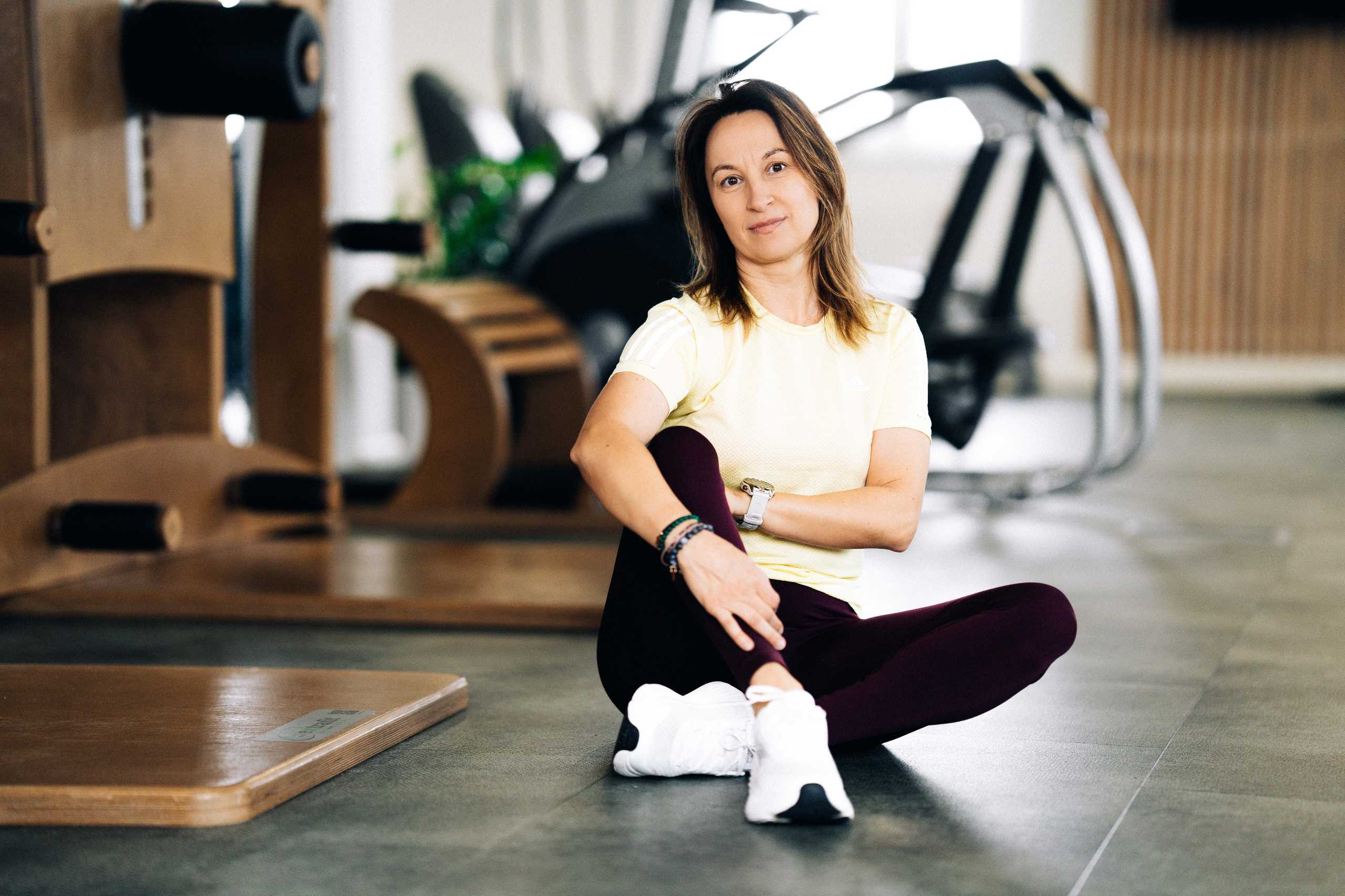 Fotografia wizerunkowa w Szczecinie — trenerka fitness w akcji, siedząca na podłodze w klubie fitness 3L.