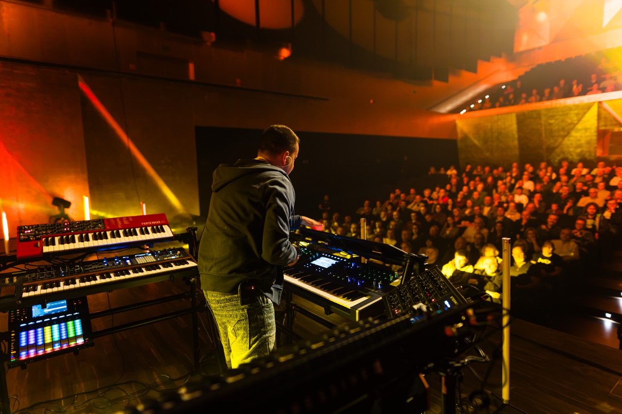 Fotografia koncertowa w Szczecinie — kompozytor Madis gra na syntezatorach przed publicznością w Filharmonii Szczecińskiej.