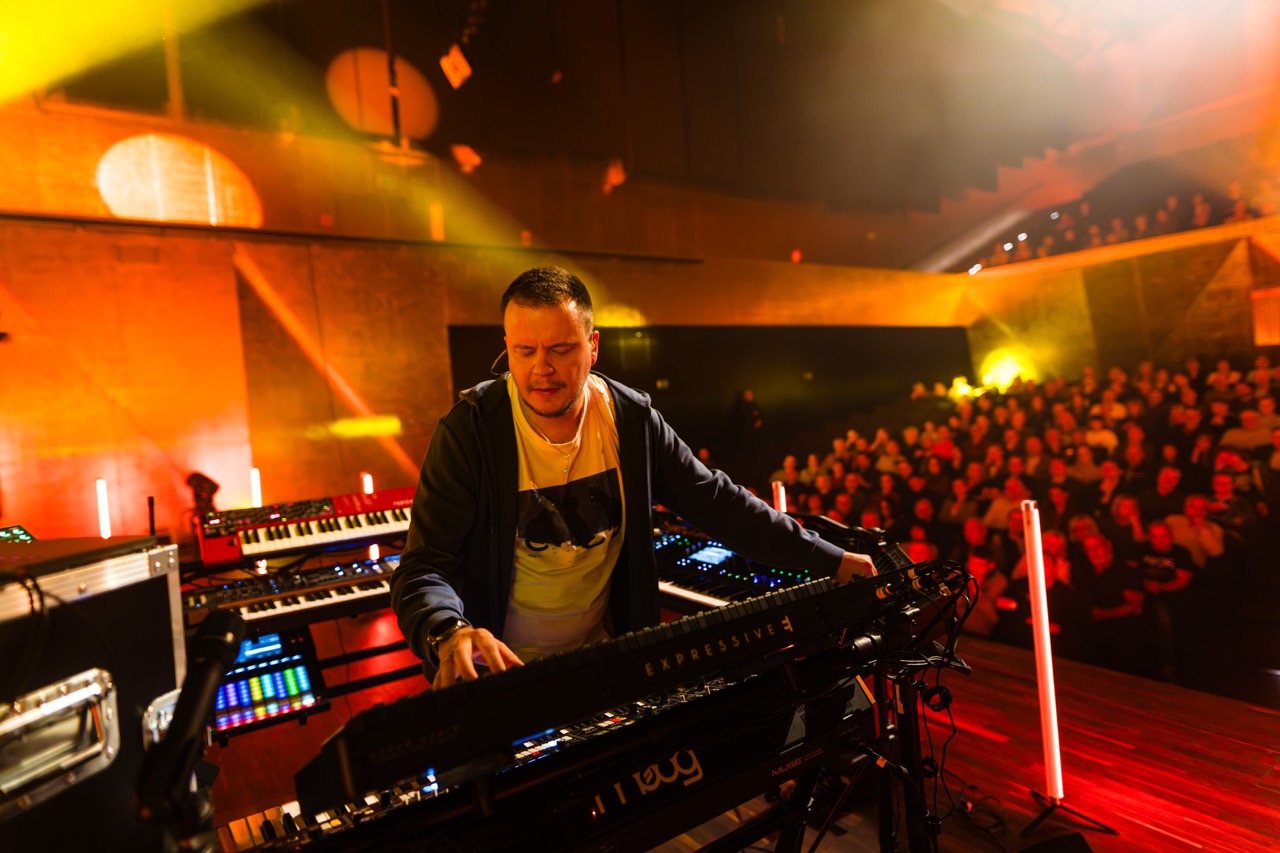 Artysta Madis podczas występu na scenie Filharmonii Szczecińskiej, z widownią w tle.