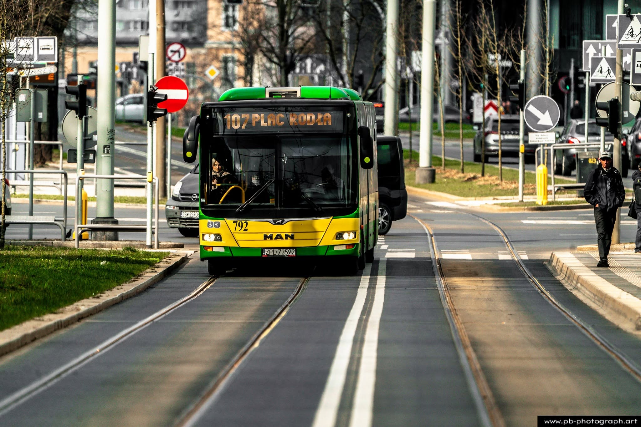 Autobus linii 107 na ulicy w Szczecinie, w tle znaki drogowe i przejście dla pieszych.