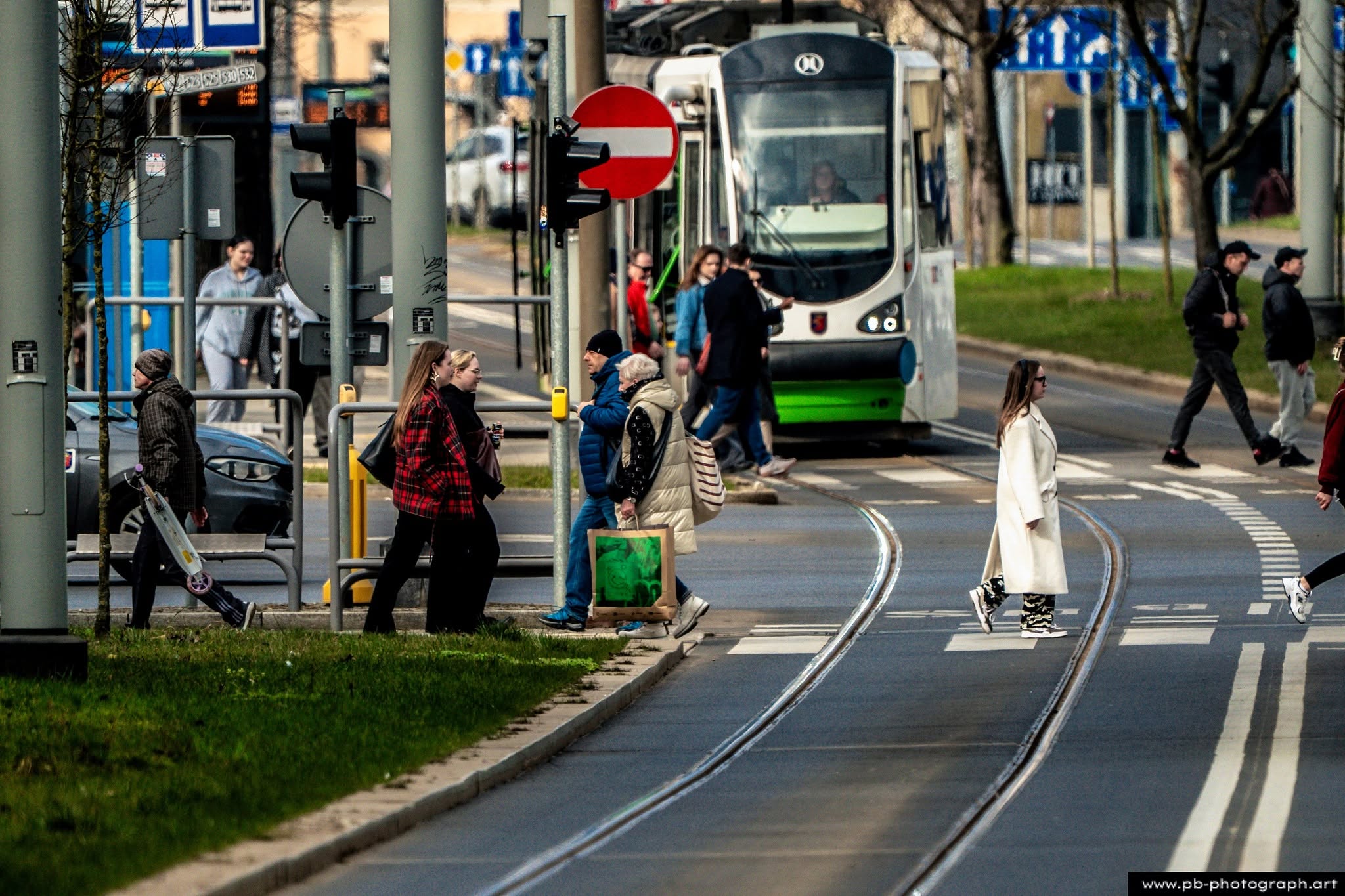Fotografia uliczna w Szczecinie — przechodnie na ulicy, tramwaj w tle, dynamiczna scena życia miejskiego.
