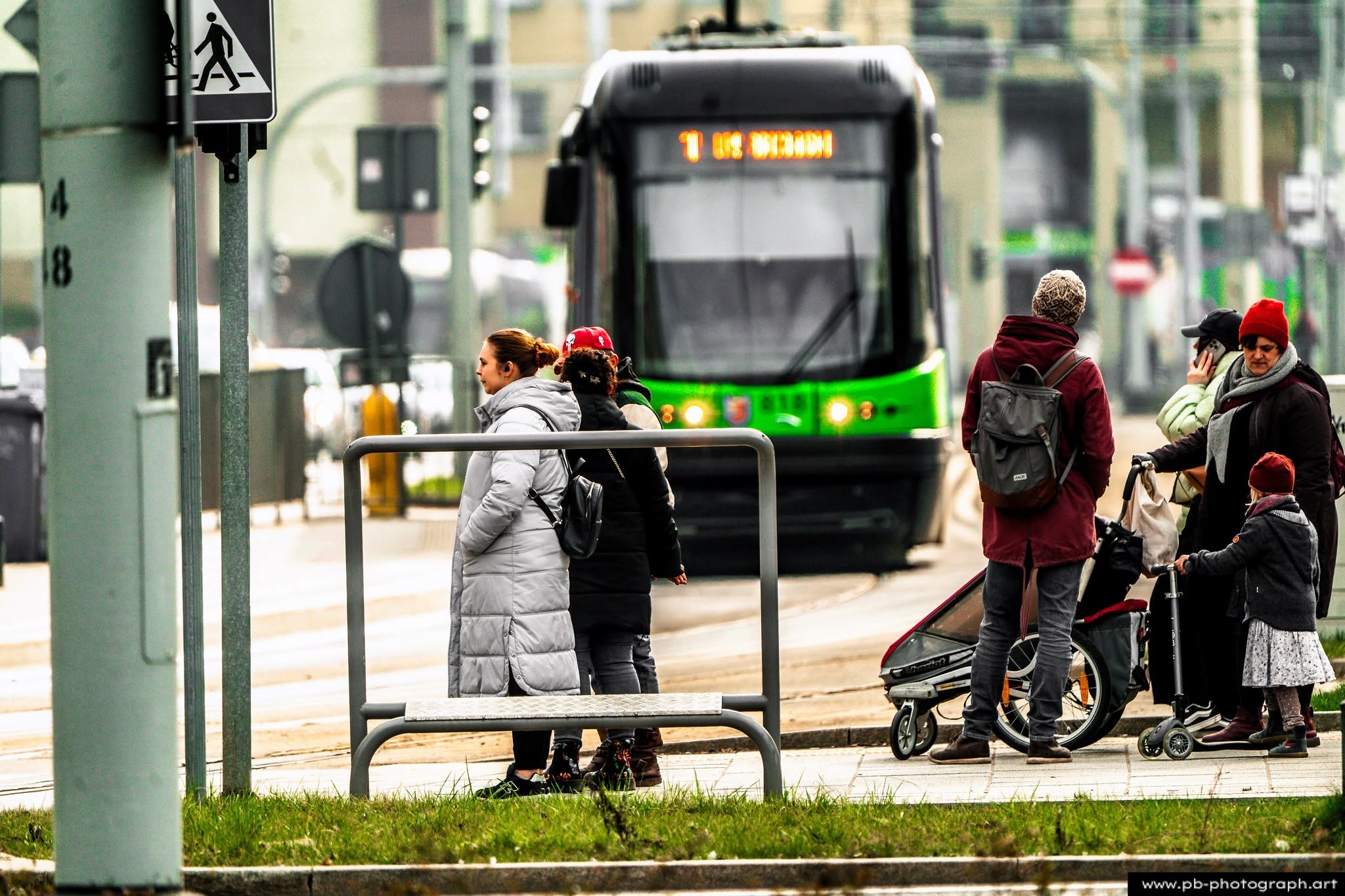 Grupa osób czekających na tramwaj na przystanku w Szczecinie, z widokiem na nadjeżdżający pojazd.