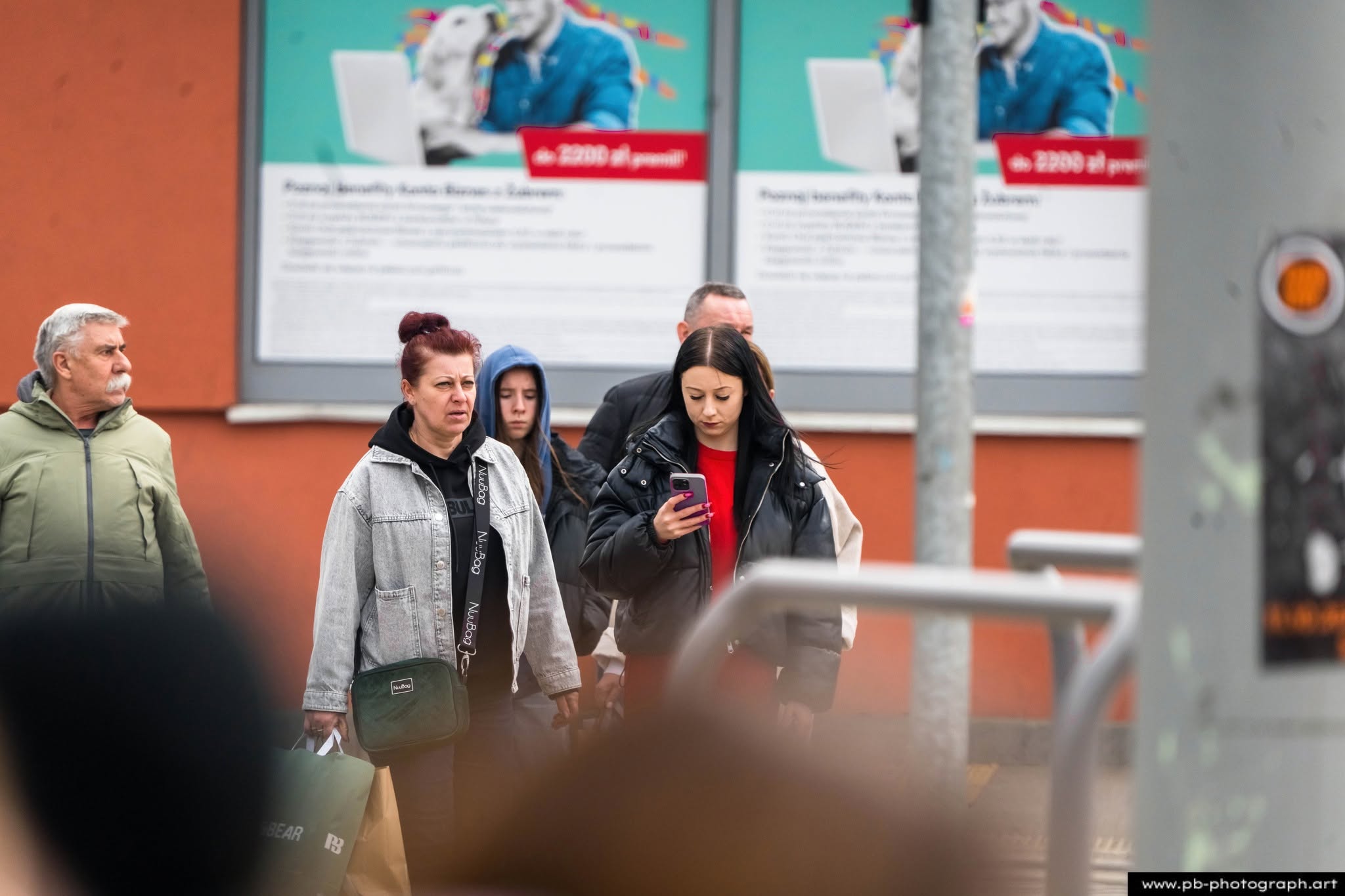 Grupa przechodniów na ulicy w Szczecinie, wśród nich kobieta z telefonem w ręku, obok mężczyzna w kurtce.