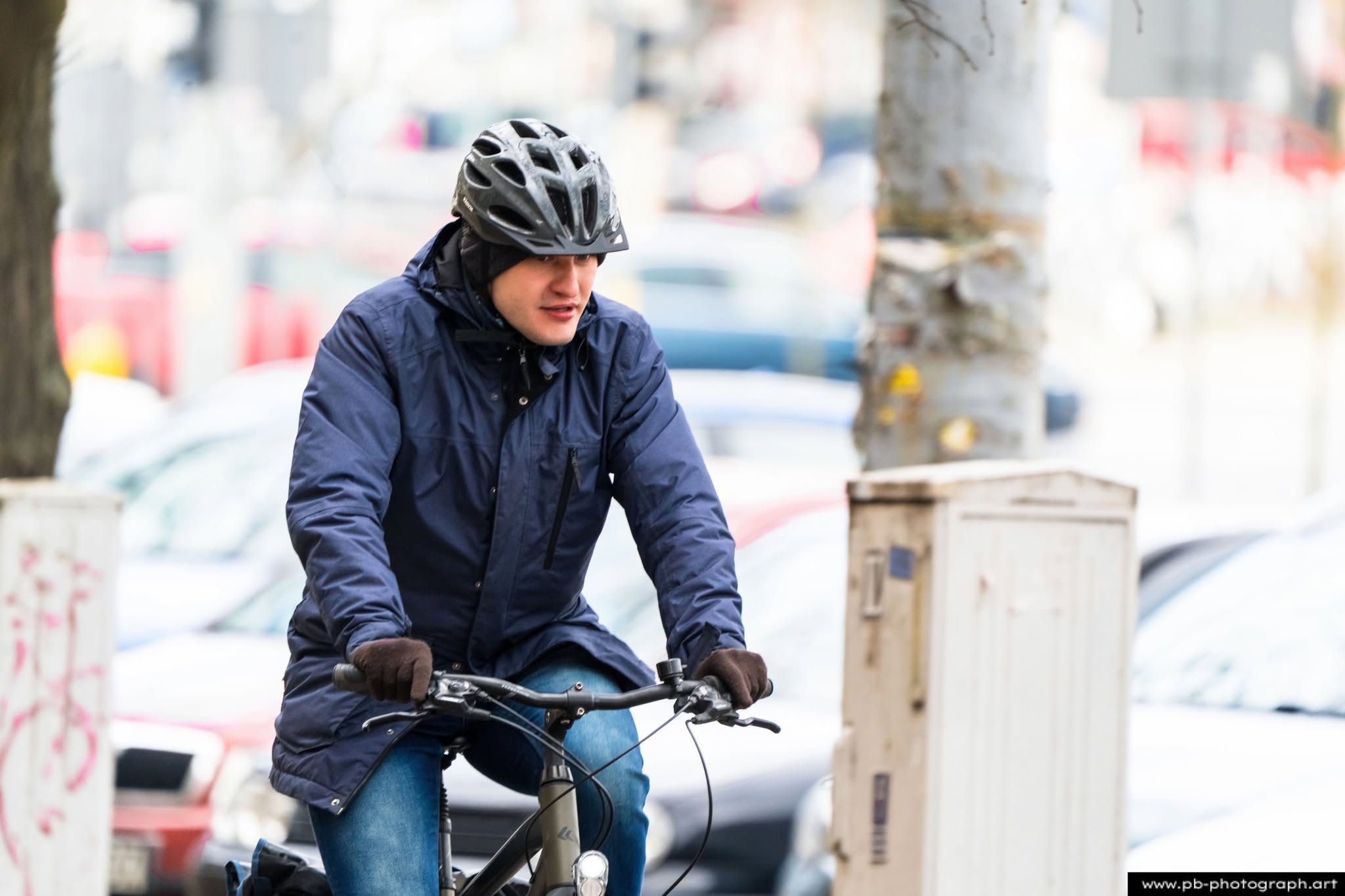 Mężczyzna na rowerze w Szczecinie, ubrany w ciepłą kurtkę i kask, jedzie ulicą w miejskim otoczeniu.