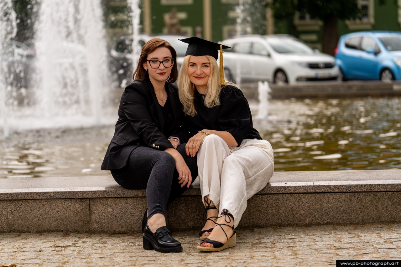 Absolutorium w Szczecinie - dwie absolwentki w togach siedzące przy fontannie w Parku Kasprowicza.