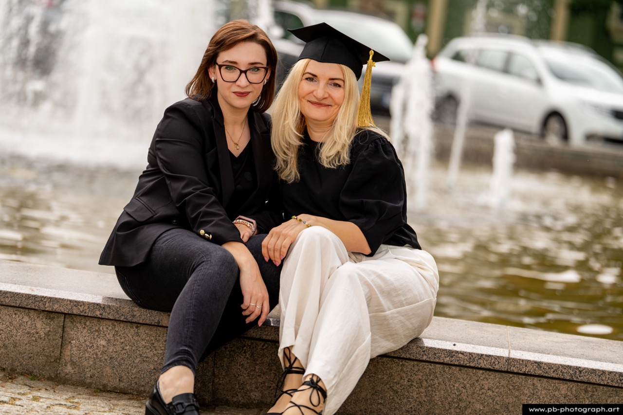 Absolutorium w Szczecinie — dwie absolwentki w togach siedzą przy fontannie w Parku Kasprowicza.