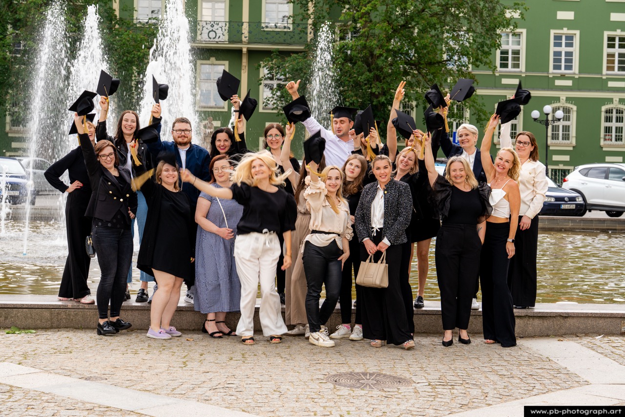 Reportaż z absolutorium w Szczecinie — grupa absolwentów świętuje przy fontannie w Parku Kasprowicza.