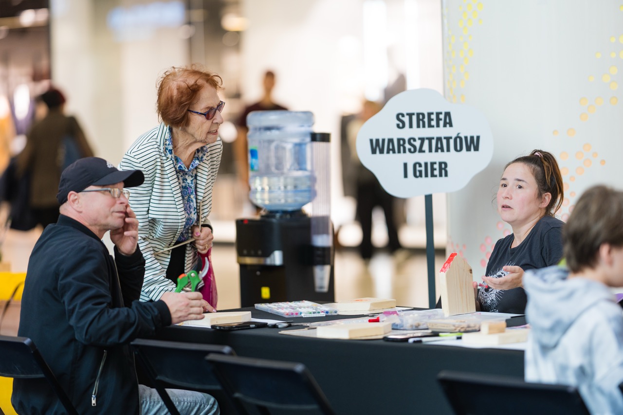 Fotografia eventowa w Szczecinie — uczestnicy warsztatów w strefie gier rozmawiają przy stole w CH Galaxy.