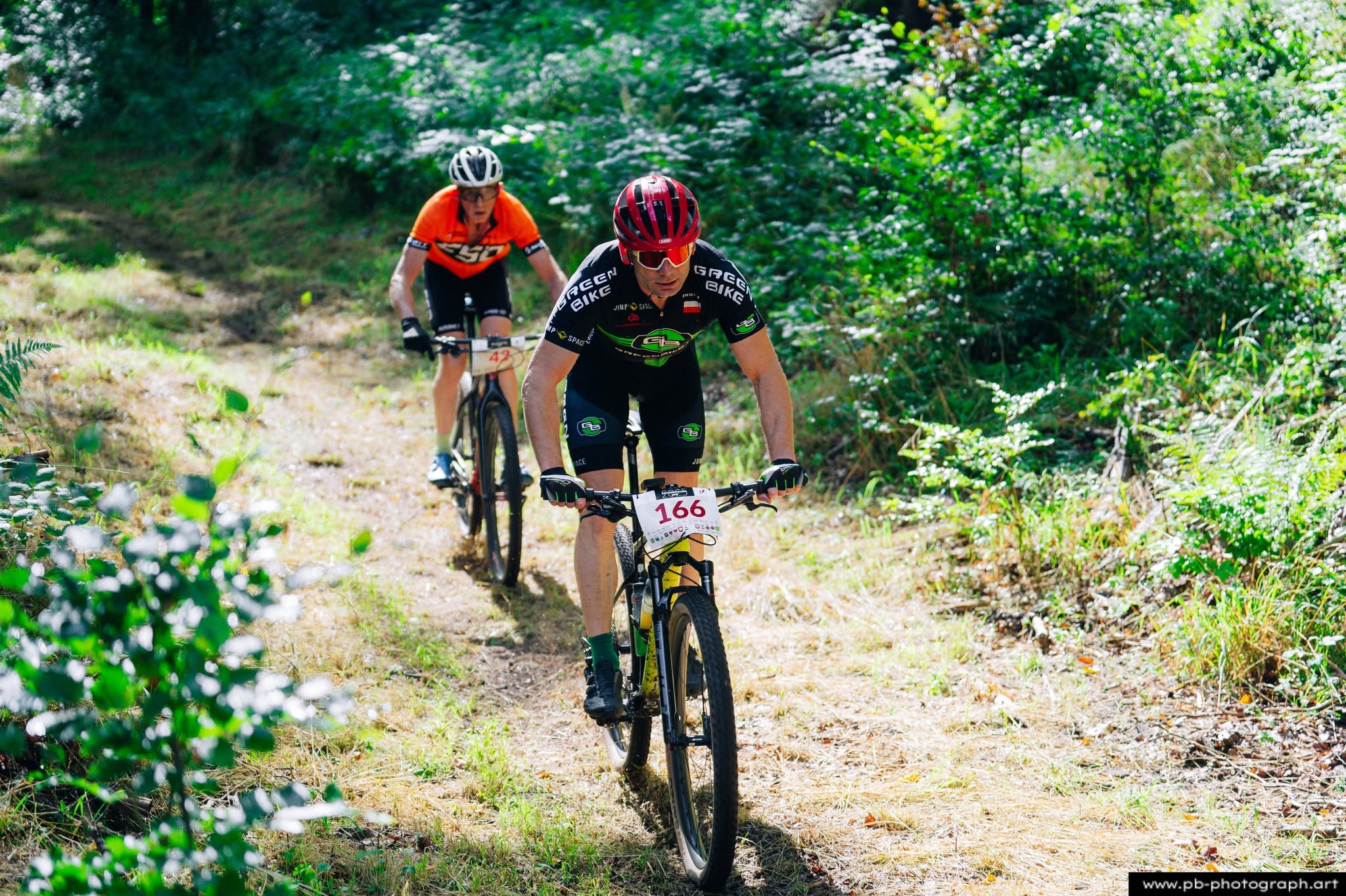 Fotografia sportowa z wyścigów MTB w Szczecinie — zawodnicy pokonują trasę w lesie.