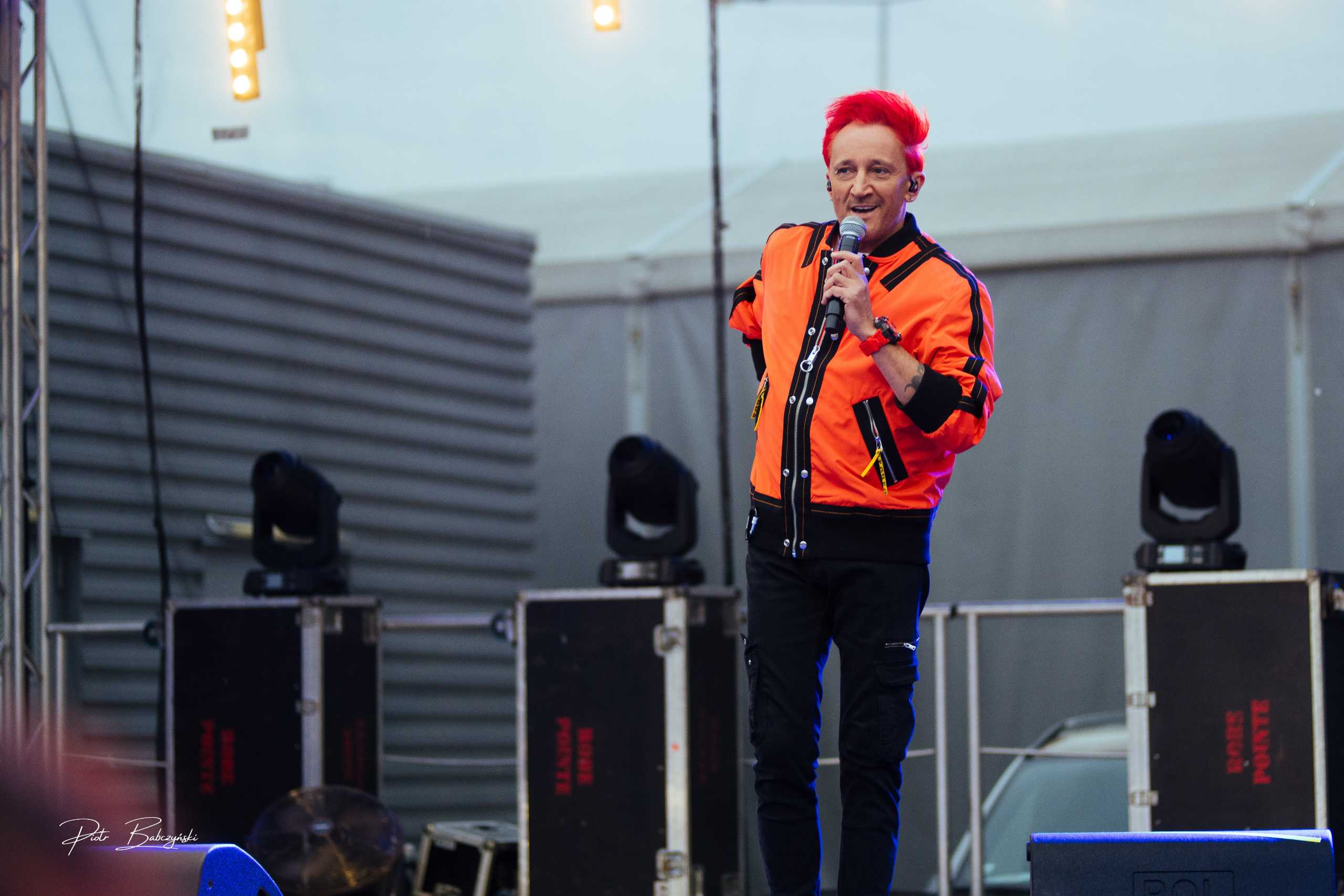 Michał Wiśniewski w pomarańczowej kurtce na scenie w Centrum PTAK EXPO podczas koncertu.