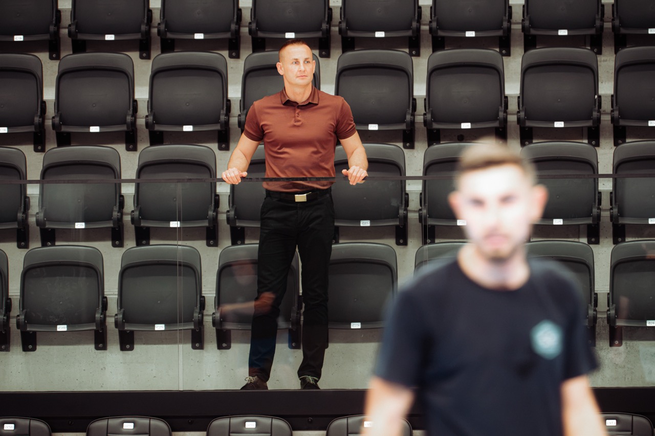 Mężczyzna stoi przy barierce na tle pustych trybun hali sportowej
