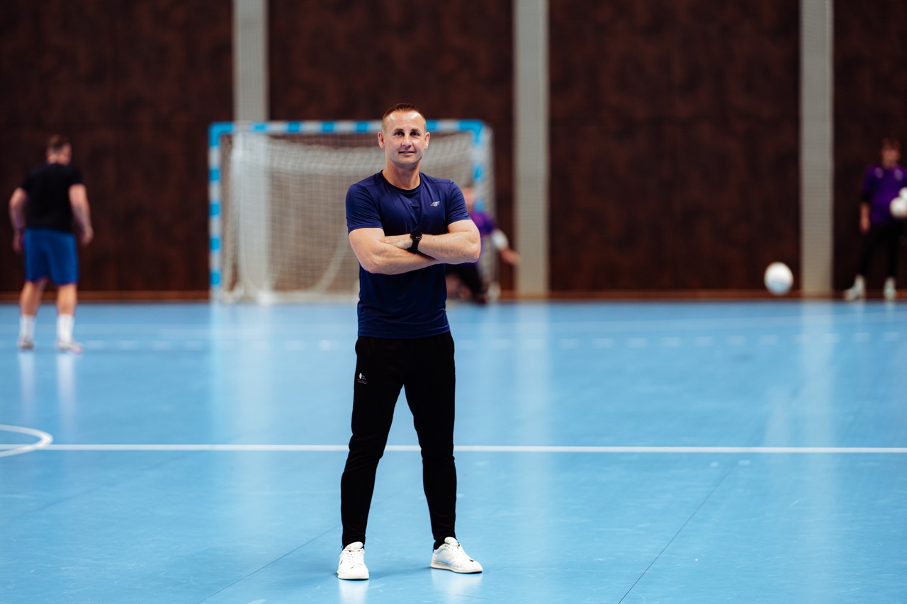 Trener z założonymi rękami stoi na środku hali futsalu