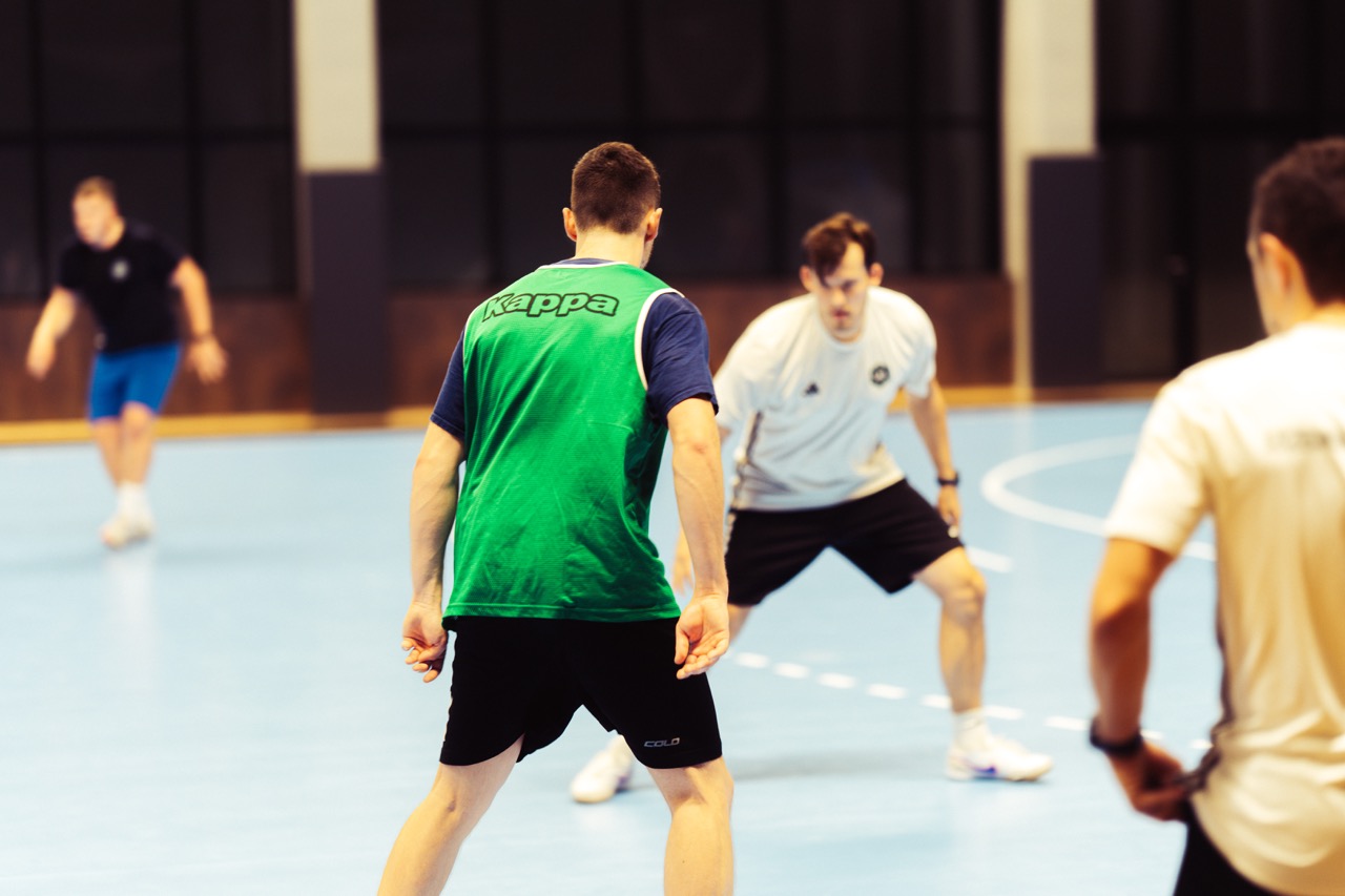 Trener mentalny prowadzi trening w Hali SDS w Szczecinie, zawodnicy w dynamicznych pozach na boisku futsalowym.