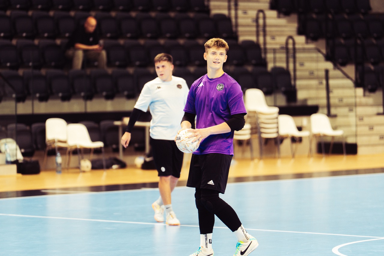 Zawodnik w fioletowej koszulce stoi z piłką na hali futsalu