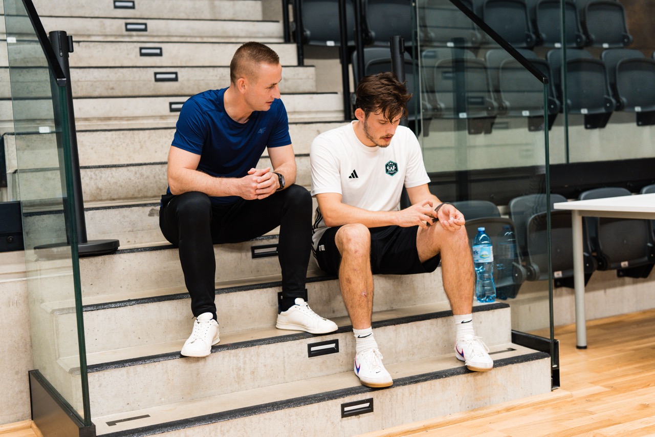 Portret dwóch zawodników Szczecińskiej Akademii Futsalu siedzących na schodach w Hali SDS, w trakcie treningu.