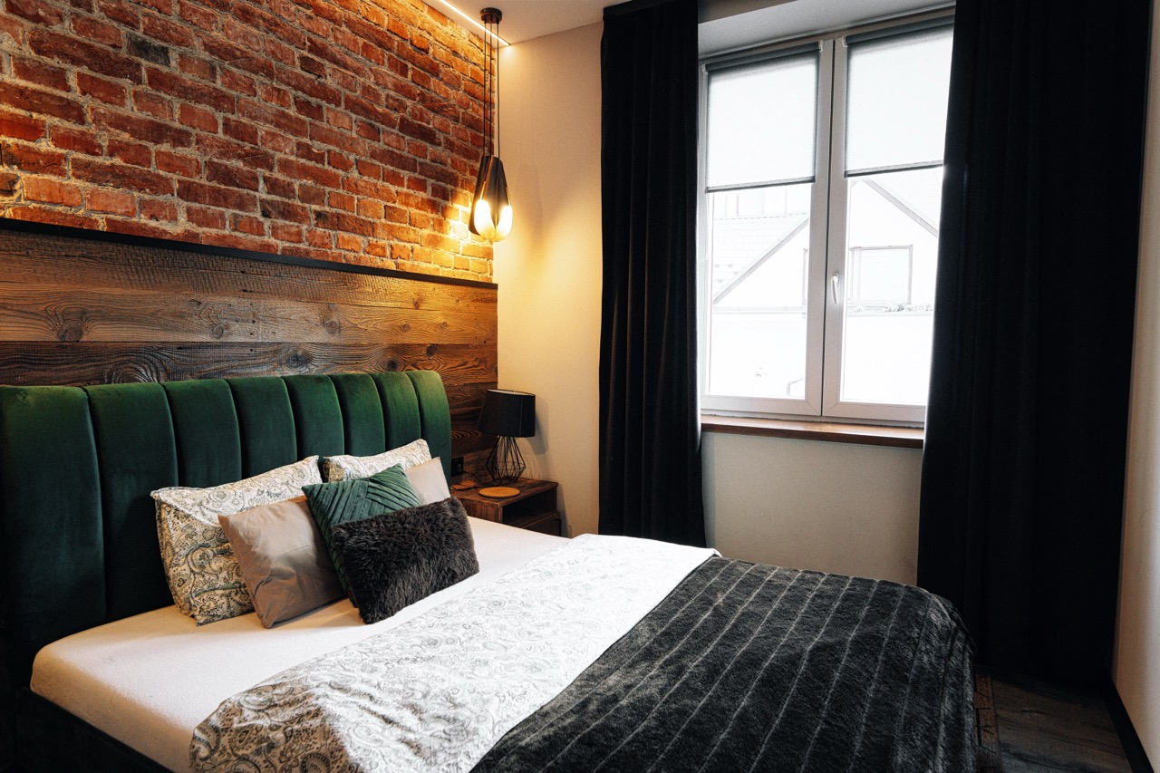 Stylowe wnętrze sypialni w apartamencie na Krupówkach z ceglaną ścianą i eleganckim oświetleniem.