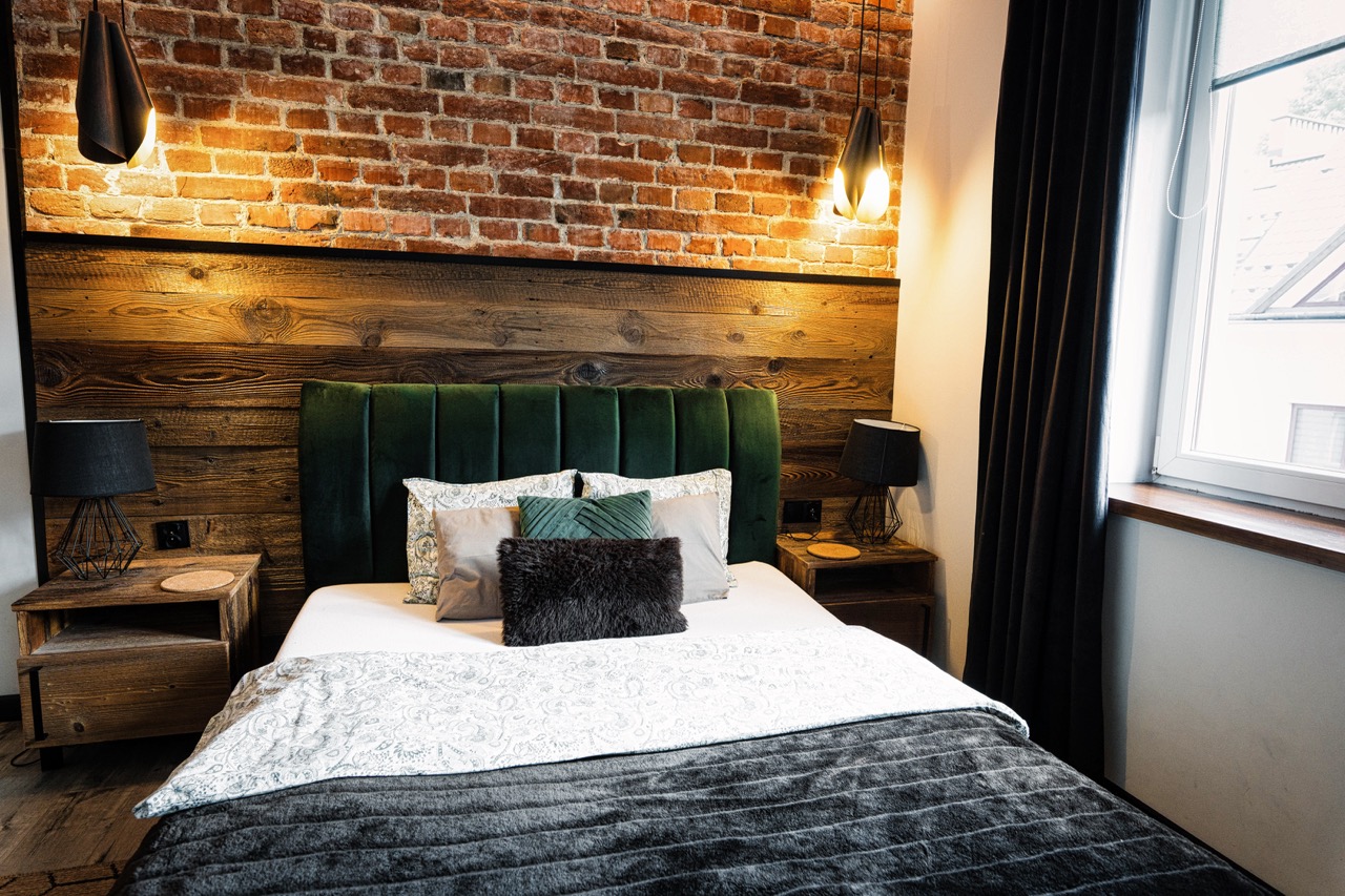 Stylowe wnętrze sypialni w apartamencie w Zakopanem z ceglaną ścianą i eleganckim łóżkiem.