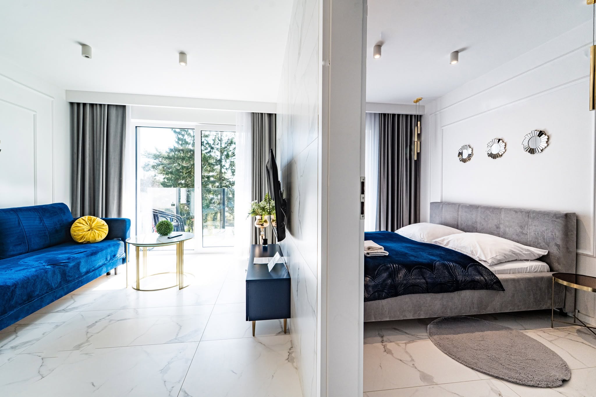Nowoczesne wnętrze apartamentu w Mielnie z widokiem na balkon, elegancka sofa i łóżko w stonowanej kolorystyce.