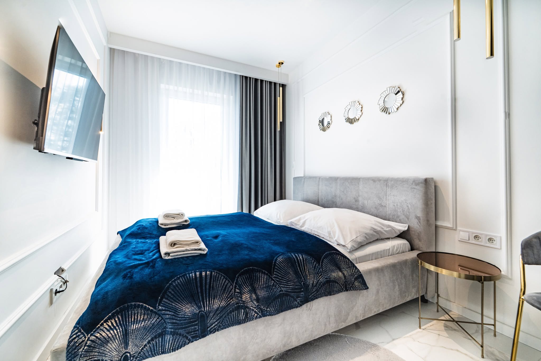 Stylowe wnętrze sypialni w apartamencie w Mielnie z niebieską narzutą i eleganckimi detalami.