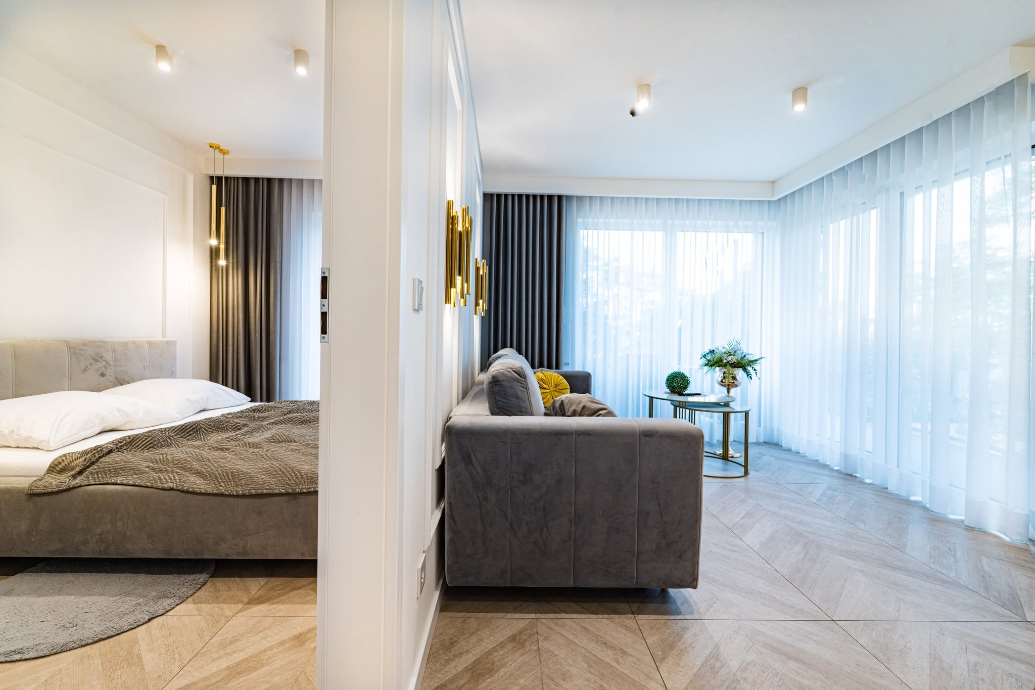 Stylowe wnętrze apartamentu w Mielnie z widokiem na salon i sypialnię, jasne zasłony i eleganckie meble.