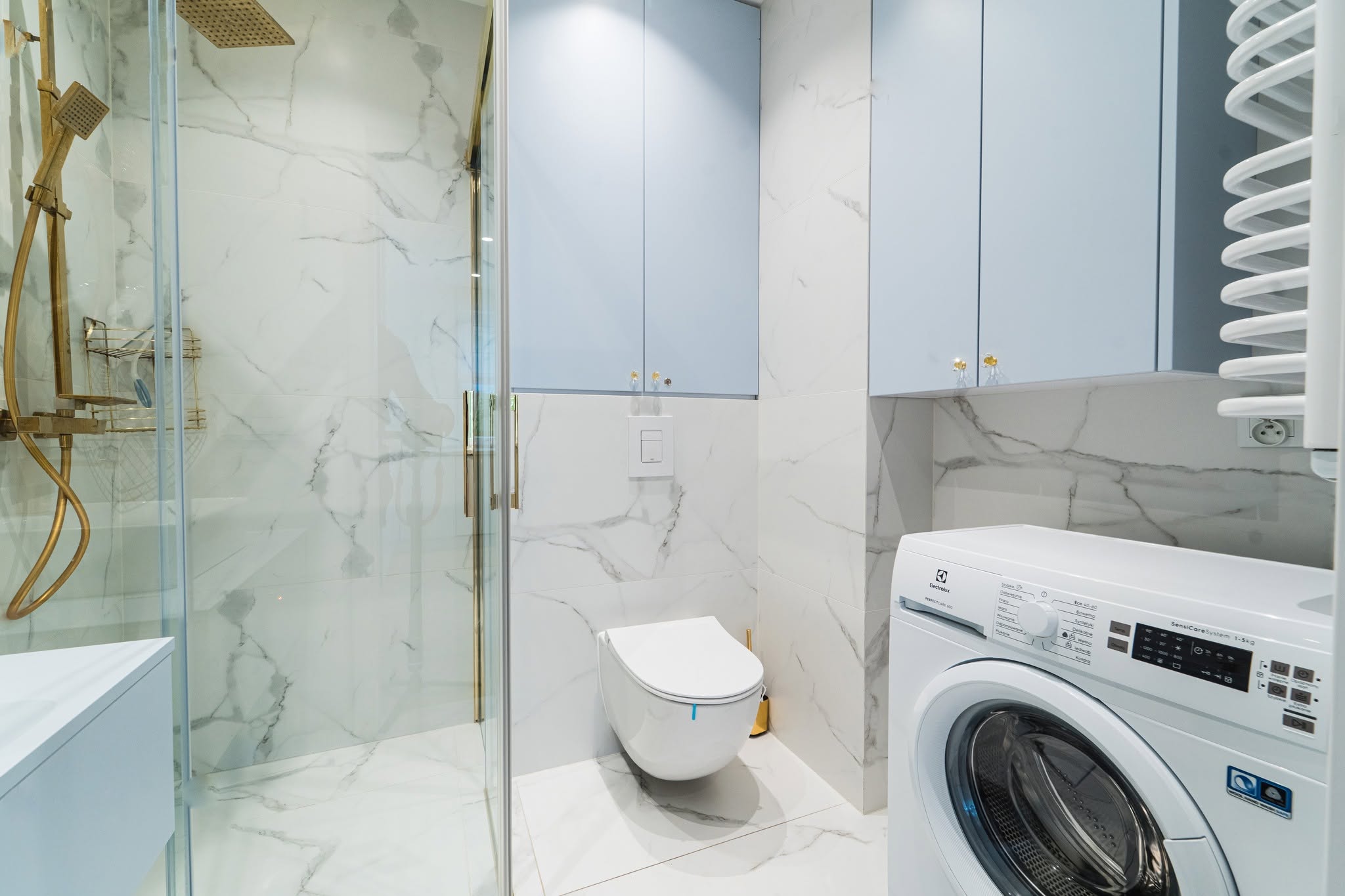 Nowoczesna łazienka w apartamencie w Mielnie z prysznicem, toaletą i pralką, wykończona w eleganckim stylu.