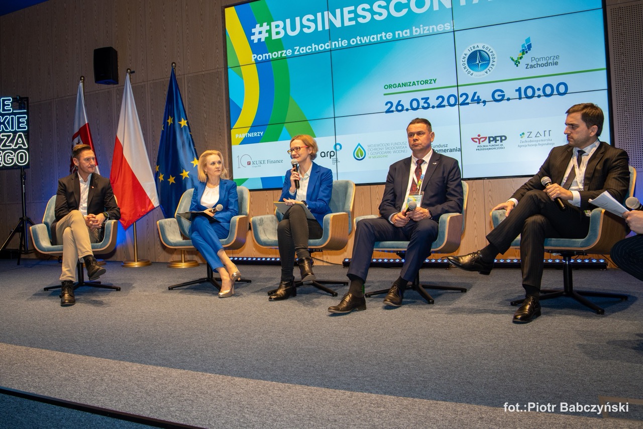 Panel dyskusyjny podczas BusinessContact6 w Szczecinie z prelegentami na scenie, w tle flagi i logo wydarzenia.