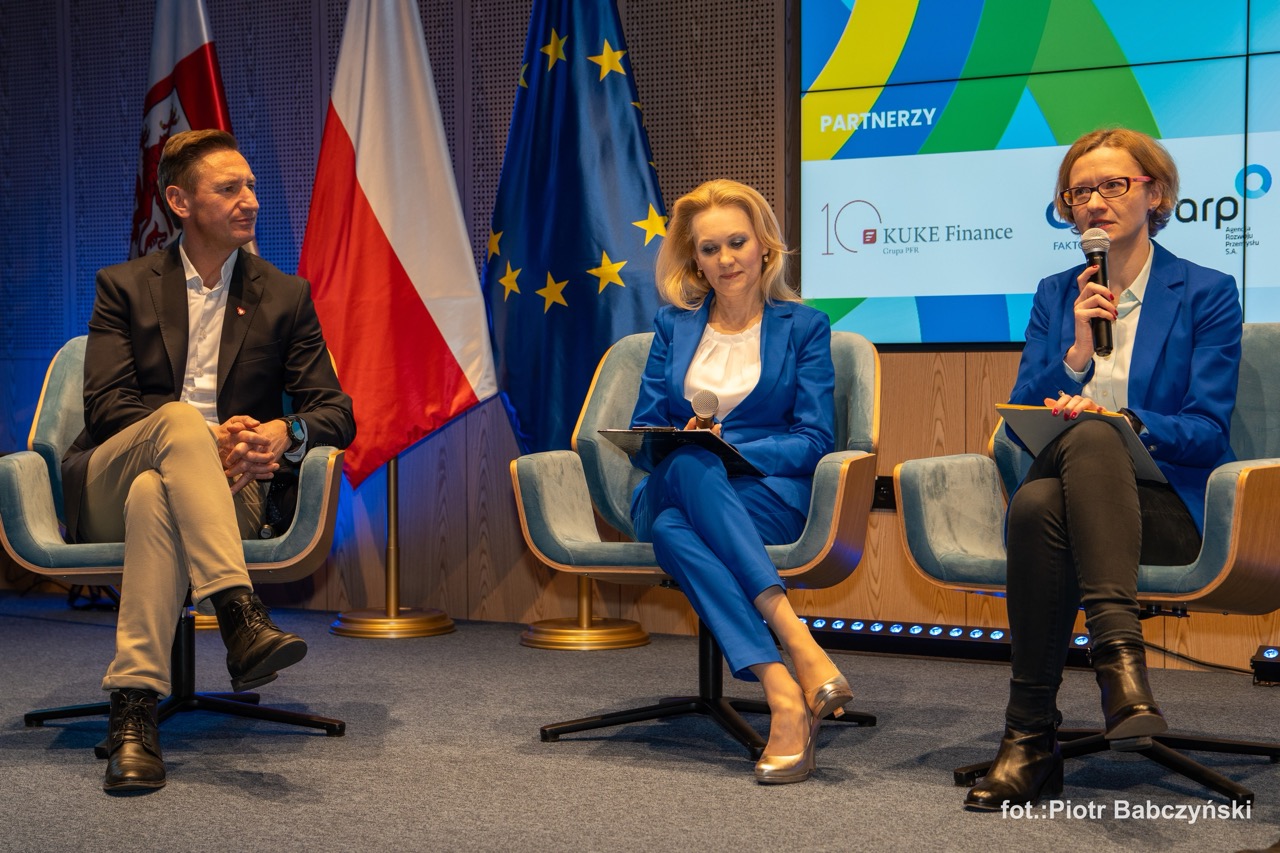 Prelegenci podczas dyskusji na scenie, z flagami Polski i Unii Europejskiej w tle, w Urzędzie Marszałkowskim w Szczecinie.