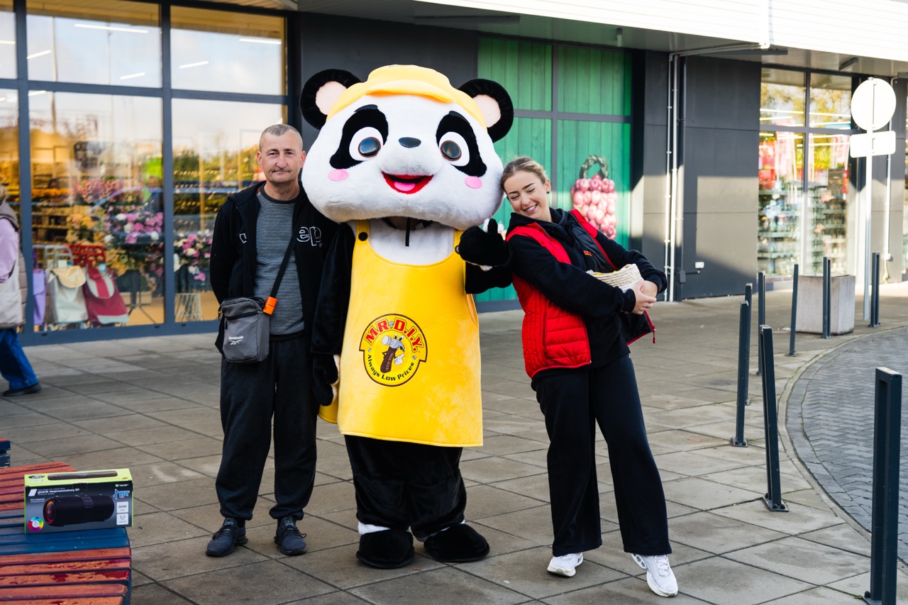 Uśmiechnięty personel sklepu MR. D.I.Y w Szczecinie pozujący z maskotką w panda na zewnątrz nowego lokalu.