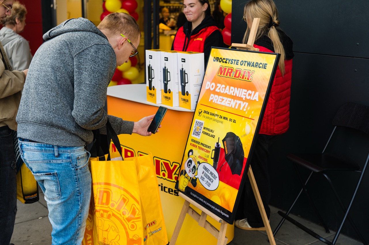 Klient z torbą MR. D.I.Y robi zdjęcie plakatu promującego otwarcie sklepu w Szczecinie.