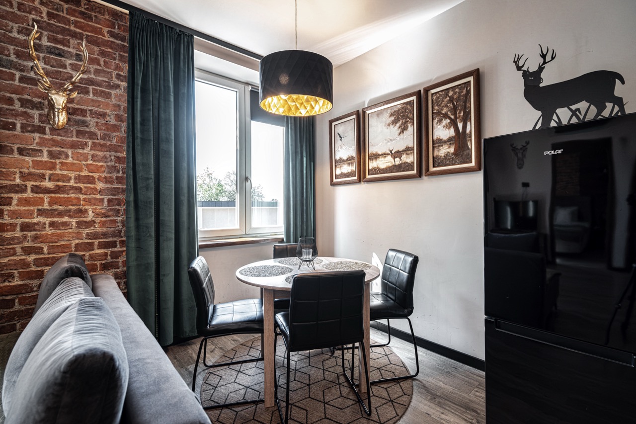 Stylowe wnętrze apartamentu w Zakopanem z okrągłym stołem, czarnymi krzesłami i dekoracjami na ścianach.