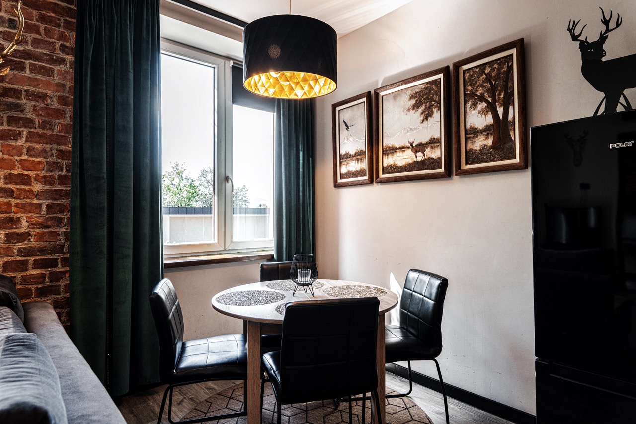 Stylowe wnętrze apartamentu w Zakopanem z okrągłym stołem i czarnymi krzesłami, na tle ceglanej ściany.