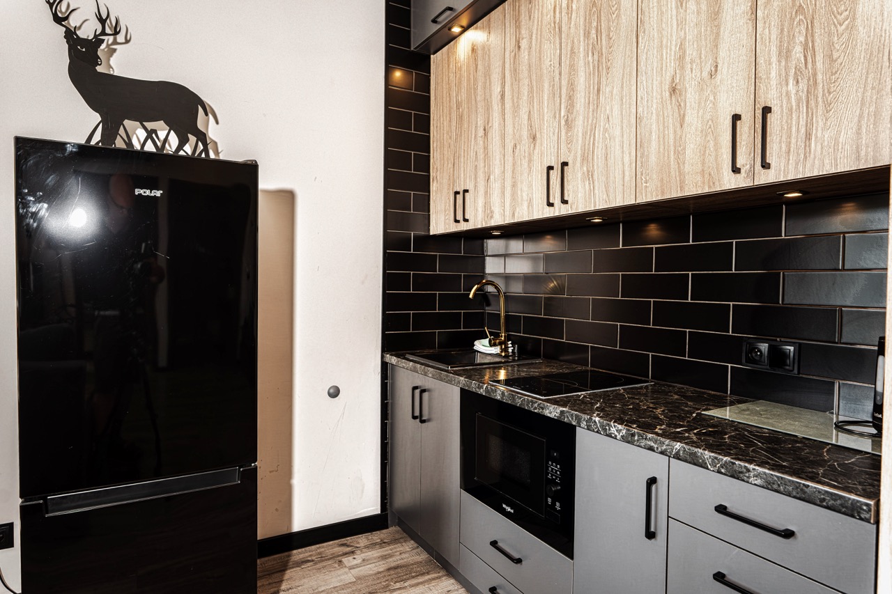 Nowoczesna kuchnia w apartamencie w Zakopanem z czarną lodówką i drewnianymi szafkami.