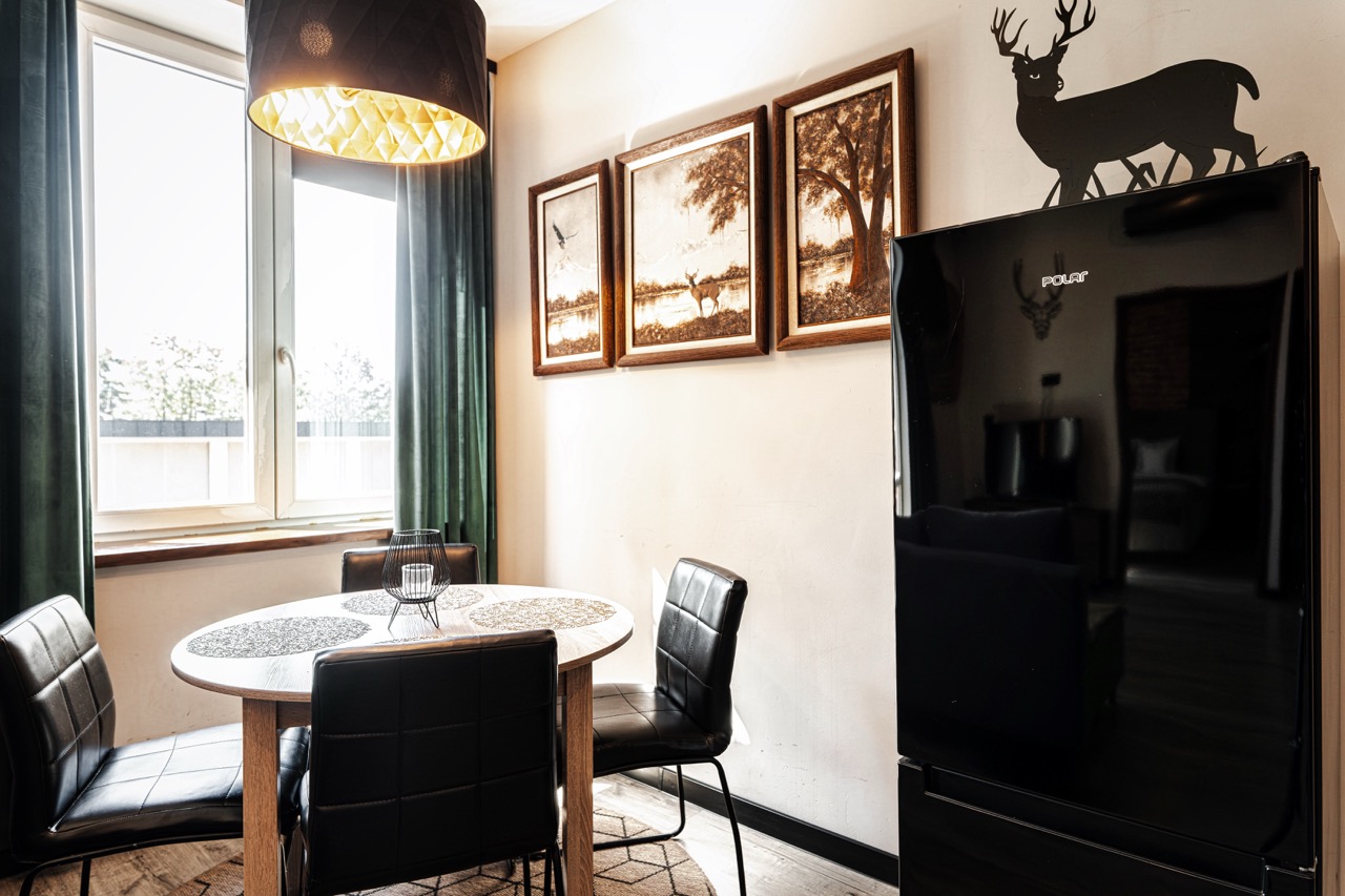 Jadalnia w apartamencie w Zakopanem z okrągłym stołem i czterema krzesłami, obok czarna lodówka i dekoracje na ścianie.