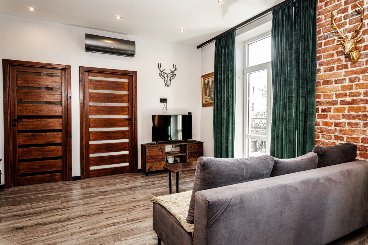 Stylowe wnętrze apartamentu w Zakopanem z ceglaną ścianą, telewizorem i elegancką sofą.