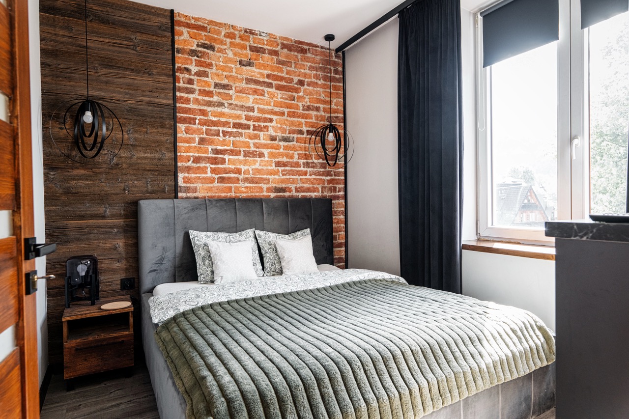 Nowoczesna sypialnia w apartamencie w Zakopanem z ceglaną ścianą i elegancką pościelą.