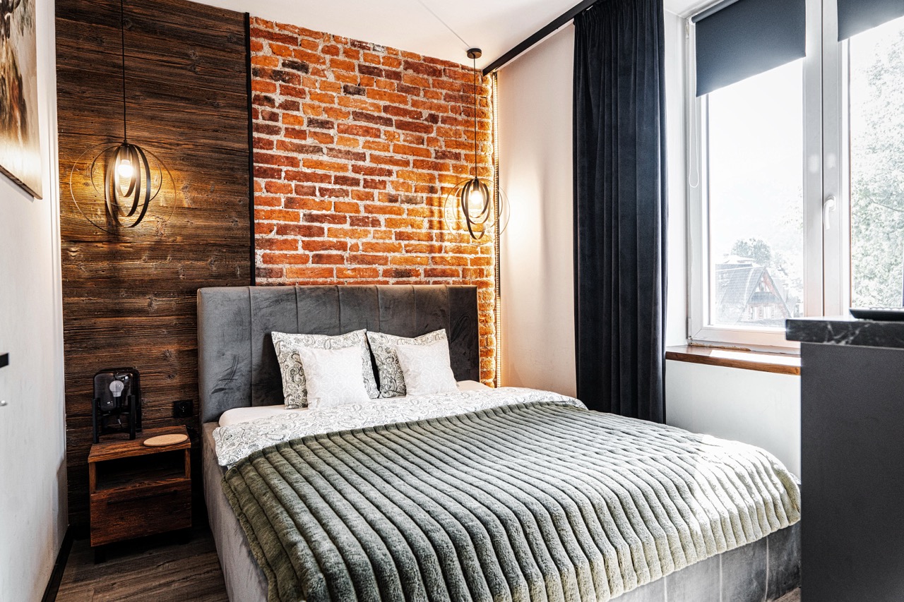 Stylowe wnętrze sypialni w apartamencie w Zakopanem z ceglaną ścianą i nowoczesnym oświetleniem.