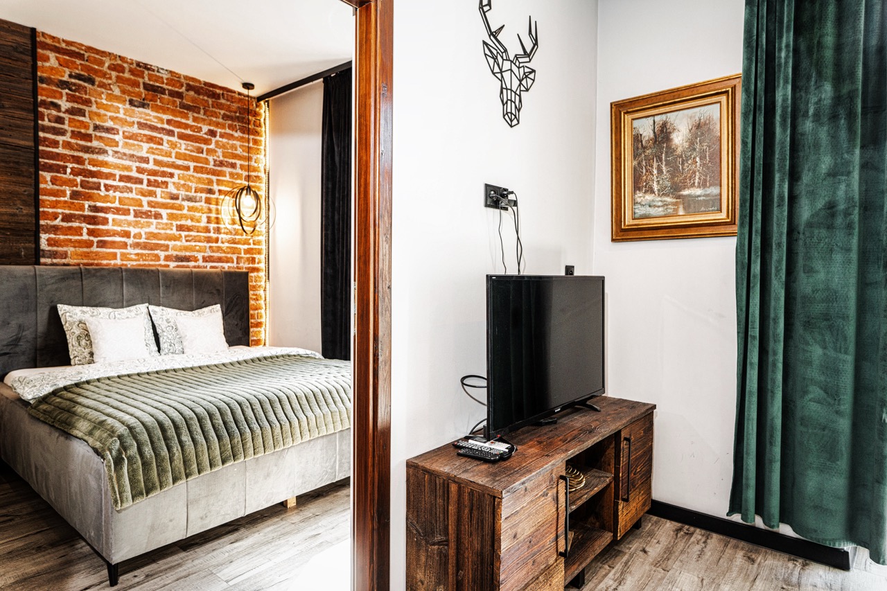 Fotografia wnętrz apartamentu w Zakopanem — sypialnia z ceglaną ścianą, telewizorem i stylowym łóżkiem.