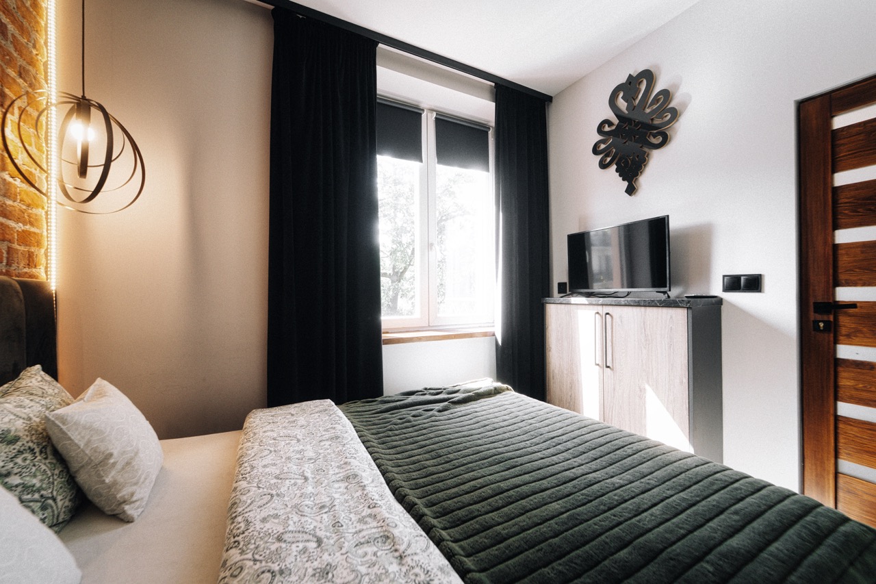 Stylowe wnętrze sypialni w apartamencie w Zakopanem z widokiem na okno, telewizorem i eleganckim oświetleniem.