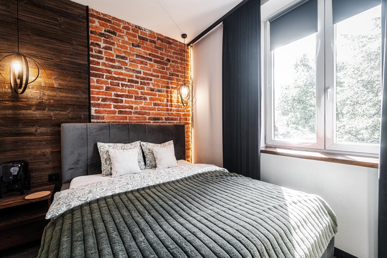 Fotografia wnętrz apartamentu w Zakopanem — stylowa sypialnia z ceglaną ścianą i eleganckim łóżkiem.
