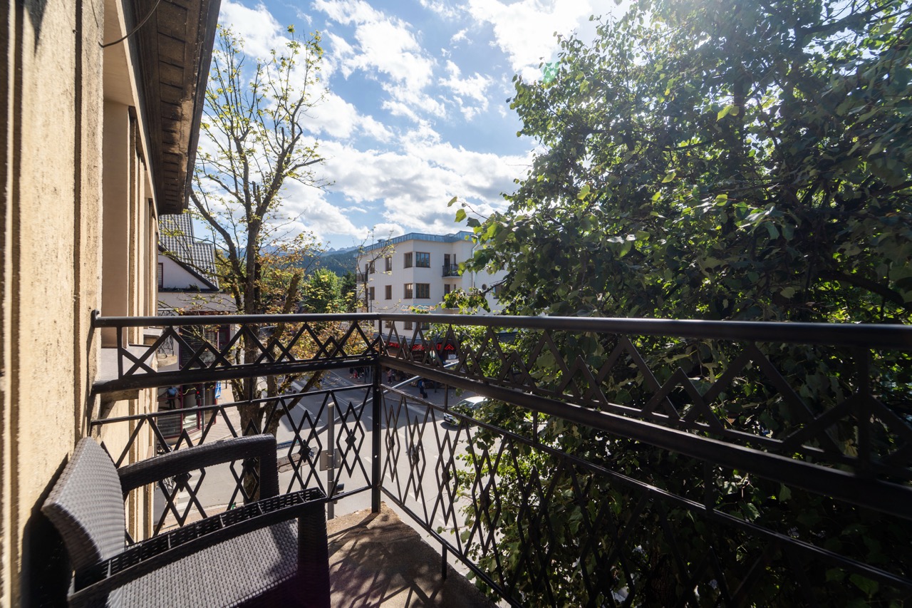 Widok z balkonu apartamentu w Zakopanem, z krzesłem i widocznymi drzewami oraz budynkami w tle.